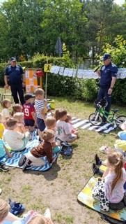policjanci rozmawiają z dziećmi, dzieci siedzą na trawie.