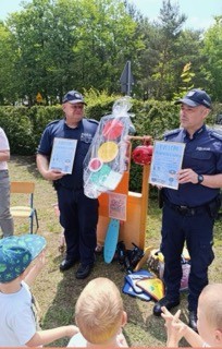 policjanci stoją przed dziećmi, trzymają w rękach dyplomy.