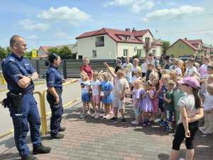 policjant i policjantka rozmawiają z dziećmi, za nimi budynki mieszkalne.