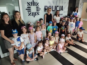 dzieci i pięć kobiet stoją w pomieszczeniu, na ścianie napis policja.