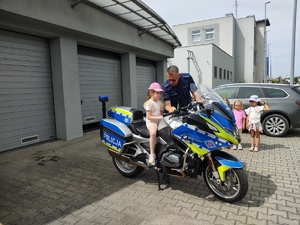 dziewczynka siedzi na policyjnym motocyklu, obok stoi policjant i dwie dziewczynki.