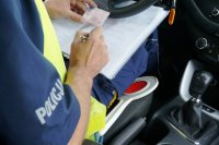 policjant trzyma w ręku blankiet prawa jazdy, siedzi w samochodzie.