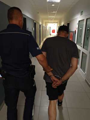 policjant trzyma mężczyznę z kajdankami na rękach trzymanych z tyłu.