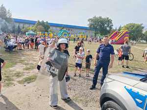 dzieci przymierzają sprzęt policyjny, obok stoi policjant, radiowóz.