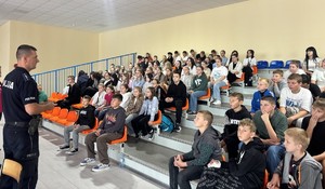 policjant rozmawia z dziećmi, które siedzą na trybunach.