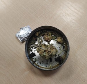 metalowe pudełko, z zawartością szaro zielonych roślin, obok zawiniątko w foli aluminiowej.