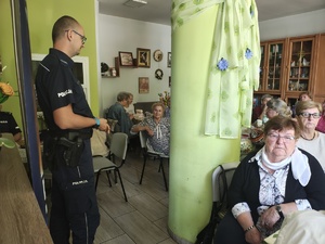 policjant rozmawia ze starszymi osobami, którzy siedzą przy stołach.