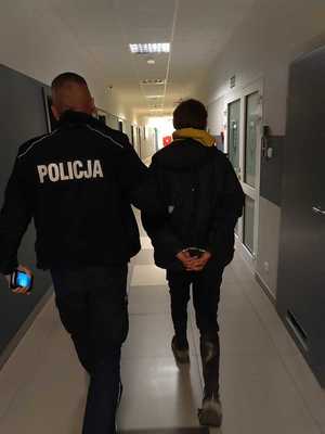 policjant prowadzi mężczyznę w kajdankach.