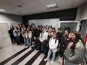 młodzież stoi na korytarzu, za nimi napis policja.