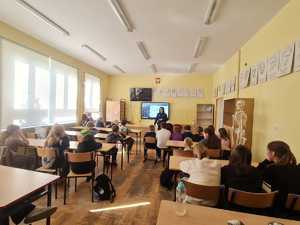 klasa szkolna, dzieci siedzą w ławkach, przed nimi stoi policjantka.