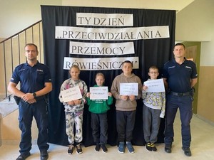 policjanci stoją z dziećmi, które trzymaja w rękach kartki.