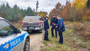 mężczyzna z mikrofonem stoi obok policjantów, radiowóz policyjny i straży leśnej.