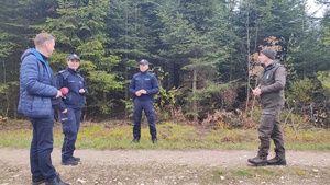 mężczyzna z mikrofonem, policjanci i strażnik leśny stoją w lesie.