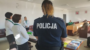 dwie kobiety w białych koszulach, policjantka, przed nimi starsze osoby.