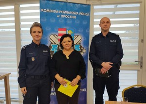 policjanci i kobieta ubrana na czarno, za nimi napis komenda powiatowa policji w Opocznie.
