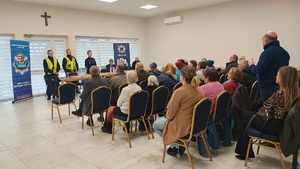 policjanci i policjantka rozmawiają z mężczyzną, =grupa ludzi siedzi na krzesłach.