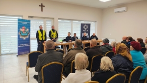 policjanci w kamizelkach odblaskowych, obok policjanci, mężczyzna, przed nimi osoby siedzą na krzesłach.