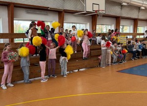 dzieci z kolorowymi pomponami mają uniesione ręce do góry.