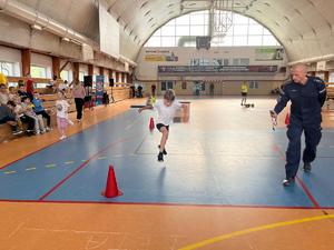 dziecko biegnie na sali gimnastycznej, obok policjant.