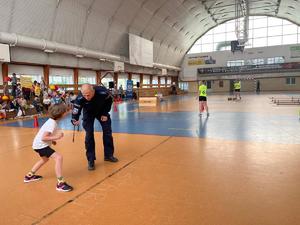 policjant pochylił się do dziecka, inne dzieci na na trybunach oraz na sali gimnastycznej.