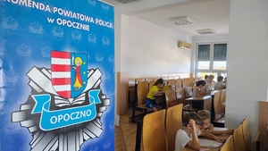 logo policji, dzieci siedzą w szkolnych ławkach.