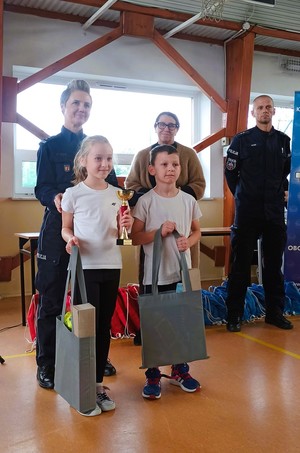 dwoje dzieci z policjantami i kobietą, dzieci trzymają puchar i torby.