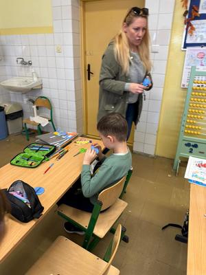 kobieta chodzi po klasie , dzieci siedzą w ławkach.