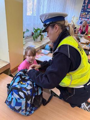 policjantka przyczepia odblask do plecaka, obok niej dziewczynka.