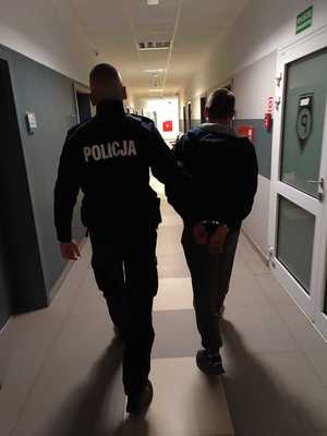 policjant prowadzi mężczyznę w kajdankach.