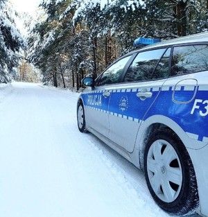 radiowóz policyjny, zaśnieżona droga, drzewa w śniegu.