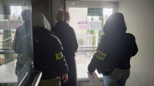 dwie policjantki stoją z kobietą, w jasnych włosach i czarnym płaszczu.