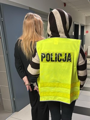 kobieta z kajdankami na rękach trzymanych z tyłu, osoba z napisem policja.