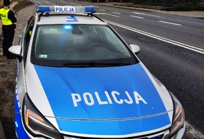 radiowóz, za nim stoi policjantka.