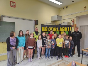 policjanci stoją w klasie z dziećmi, za nimi tablica.