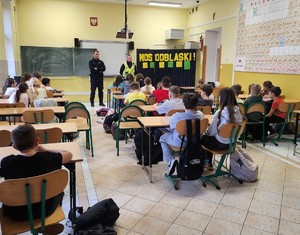 policjanci stoją przed dziećmi, dzieci siedzą w ławkach, klasa lekcyjna.