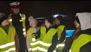 dzieci w kamizelkach odblaskowych z policjantem.