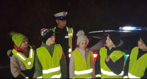 dzieci z policjantem, wszyscy w kamizelkach odblaskowych.
