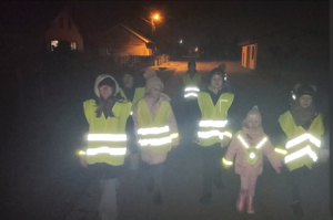 dzieci w kamizelkach odblaskowych, idą wieczorem.