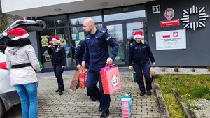 policjanci i kobieta noszą prezenty do samochodu.