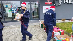 policjanci noszą prezenty , za nimi budynek, na głowach czerwne czapki.
