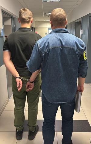 mężczyzna w kajdankach z mężczyzna w niebieskiej koszuli z napisem policja.