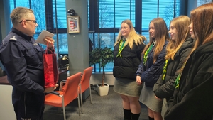 policjant z harcerkami, w ręku trzyma torebkę i kopertę.