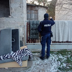 policjant w mundurze zagląda przez płot.obok budynki.