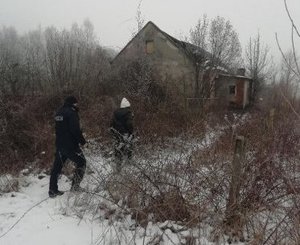 policjant i kobieta idą po śniegu w kierunku opuszczonego budynku.