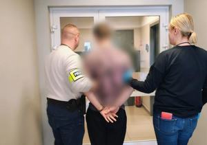 mężczyzna i kobieta prowadzą mężczyznę w kajdankach, na ręce jednego z mężczyzn napis policja.