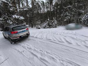 radiowóz policyjny stoi w lesie, śnieg, drugi samochód osobowy.