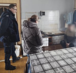 Policjant z pracownikiem GOPS rozmawia z mężczyzną w pomieszczeniu kuchennym.