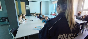 policjantka stoi przed dziećmi siedzącymi przy stołach.