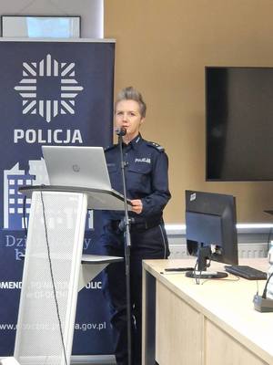 policjantka mówi do mikrofonu, za nią napis policja.