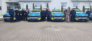 cztery radiowozy oznakowane, pomiędzy nimi stoją osoby w cywilnych ubraniach i w mundurach policyjnych.